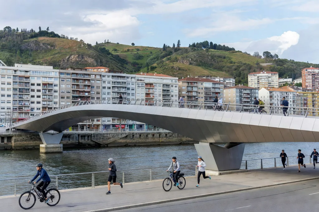 Bilbao riverside with a modern metallic pedestrian bridge, hills and apartment blocks behind