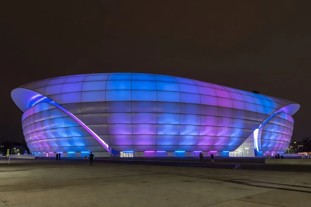 Modern German football arena with a smooth inflated-panel facade glowing in coloured exterior lighting at night