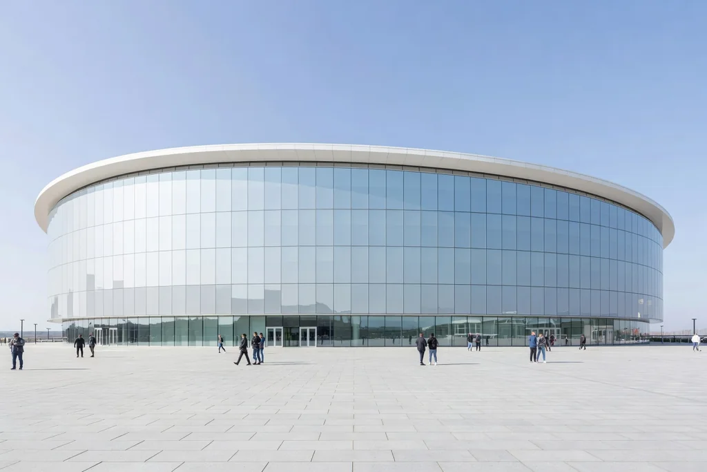 Modern English football stadium exterior in bright daylight: smooth glazed facade, curved white roof edge