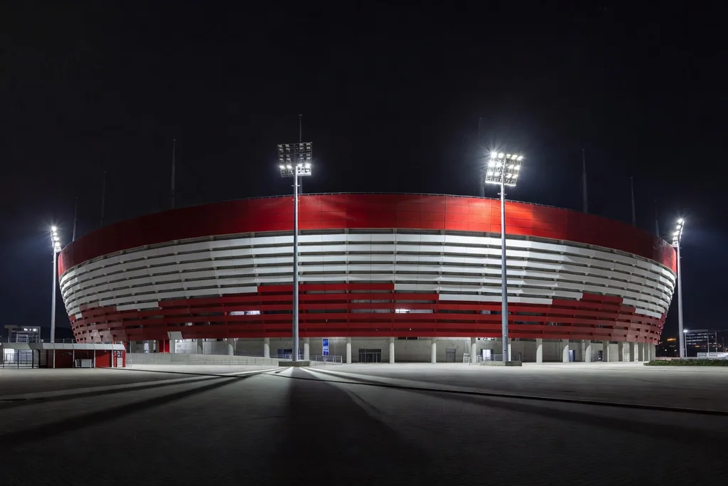 Modern Hungarian national football stadium with a bold red and white exterior and glowing floodlights at night