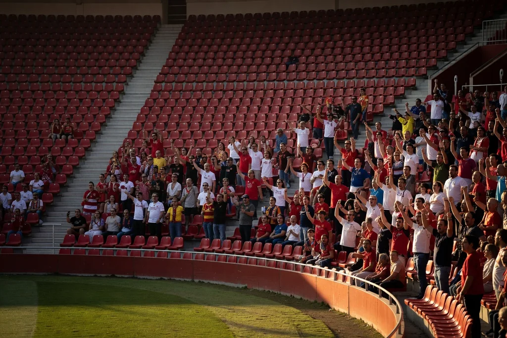 Spanish football ground with a tight tiered bowl and red seats, warm evening light, dense crowd of supporters