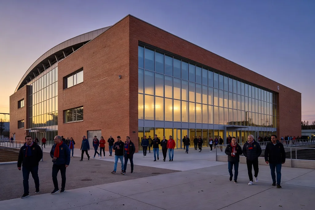 Modern Spanish football stadium with a brick-and-glass facade and a glowing interior at dusk, supporters arriving